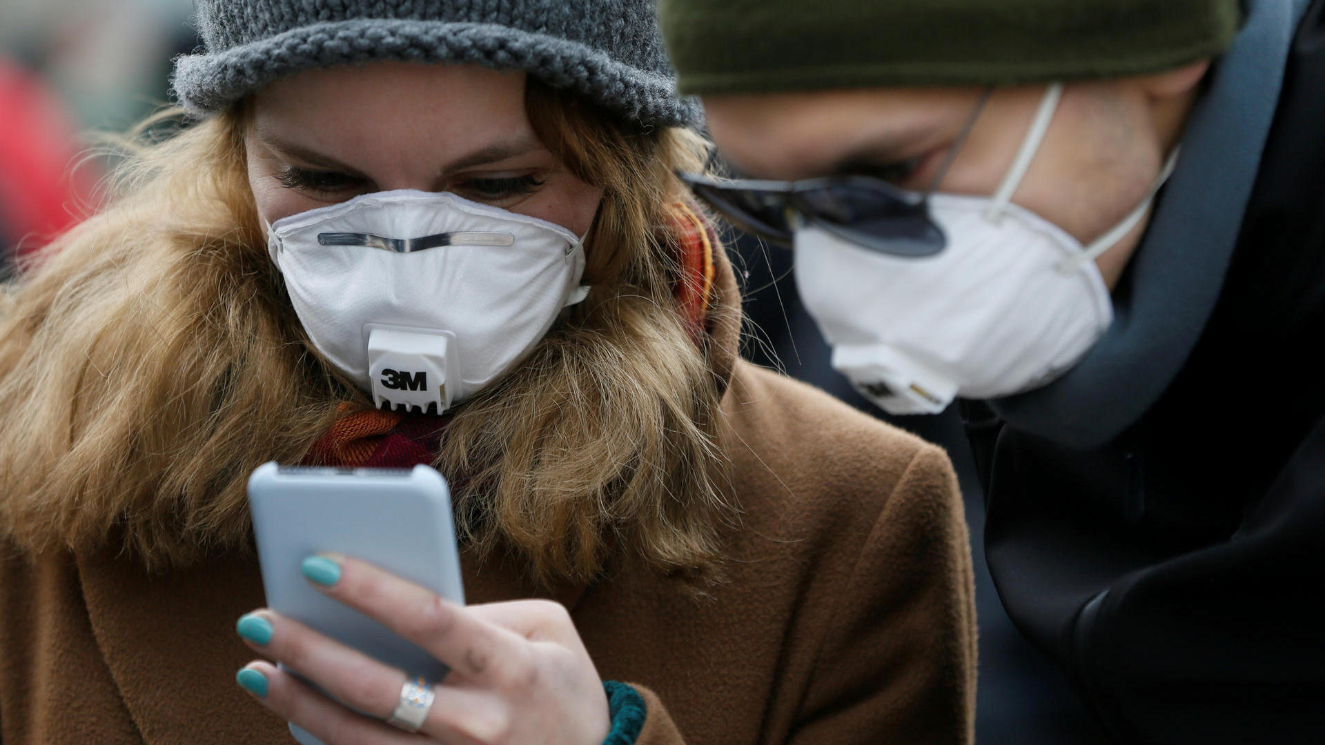People wearing protective face masks use a smartphone on a street in Kiev